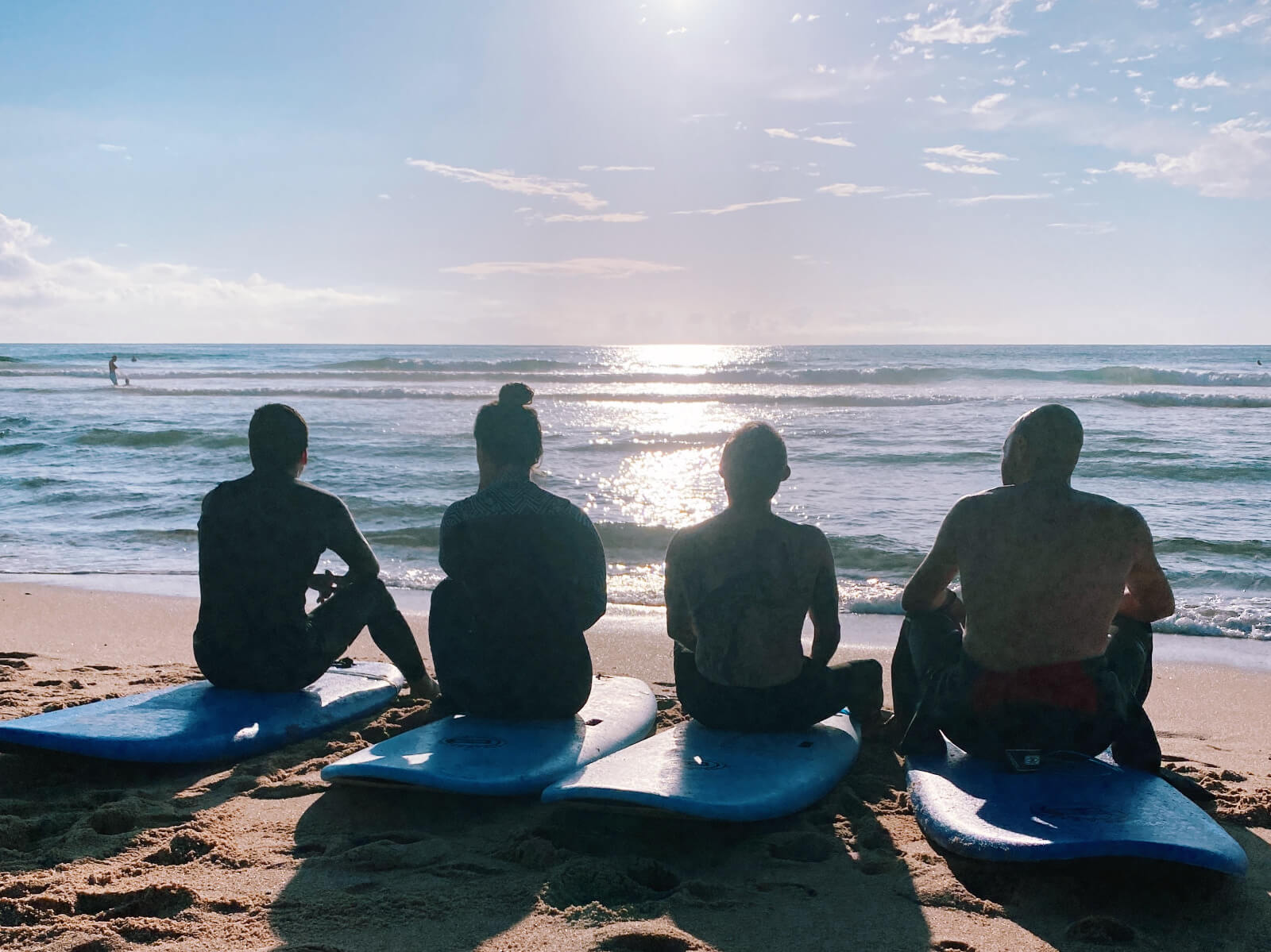 4 people sitting on a surfboard watching the ocean